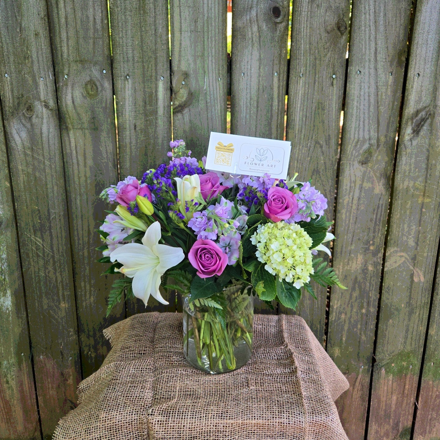Bouquet of flowers in a vase on a burlap-covered table with a wooden fence background