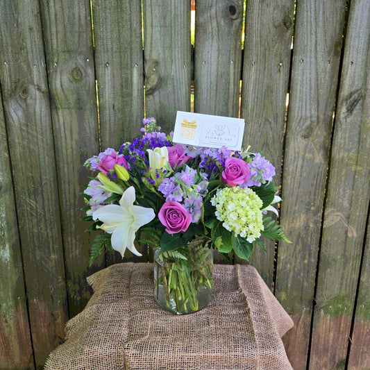 Bouquet of flowers in a vase on a burlap-covered table with a wooden fence background